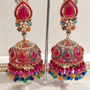 May include: A pair of gold earrings with red, pink, green, blue, and orange beads. The earrings have a bell-shaped design with a large red stone in the center.