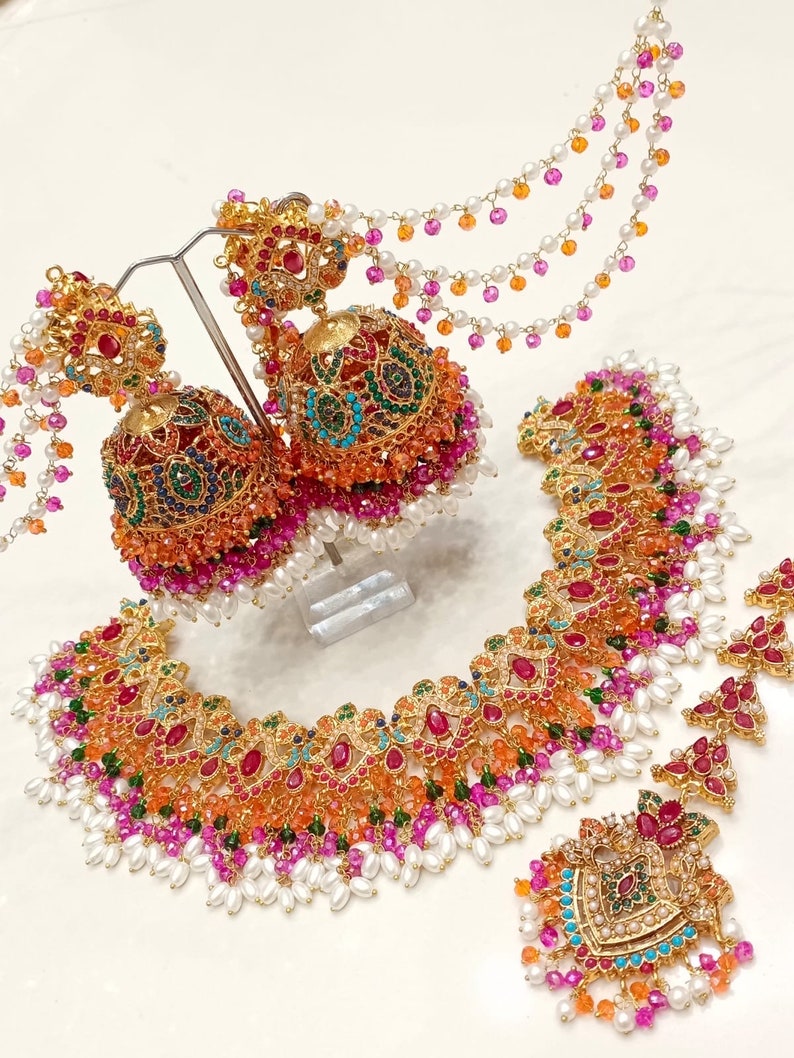 Peut inclure: Un ensemble de collier et de boucles d'oreilles en or avec des motifs complexes et des pierres pr&eacute;cieuses color&eacute;es. Le collier pr&eacute;sente un design multicouche avec des perles roses, orange, vertes et bleues. Les boucles d'oreilles sont de style pendantes avec un design et une palette de couleurs similaires.