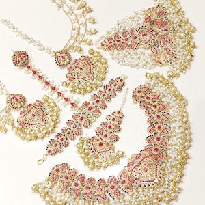 Könnte beinhalten: Ein traditionelles indisches Braut-Schmuckset mit einer goldenen Halskette mit roten und blauen Edelsteinen, Perlen und aufwendigen Blumenmustern. Das Set enthält auch Ohrringe, ein Maang Tikka und eine mehrreihige Halskette.