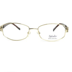May include: Gold-toned eyeglasses with a rectangular frame and brown temples. The lenses are clear, and the text "Splendor DEMO LENS ONLY" is printed on the right lens. The glasses have a classic, elegant design.