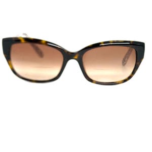 May include: Tortoiseshell sunglasses with brown gradient lenses. The frames have a classic cat-eye shape. The sunglasses are set against a white background.
