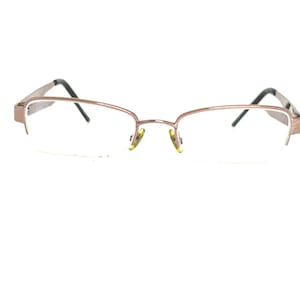 May include: A pair of eyeglasses with a light brown metal frame and clear lenses. The frame has a rectangular shape with a thin, delicate design. The temples are dark gray and the nose pads are yellow.