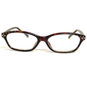 May include: Tortoiseshell-patterned eyeglasses with a cat-eye shape. The frames have small, clear rhinestones at the outer corners and along the temples. The lenses are clear, and the glasses are set against a white background.