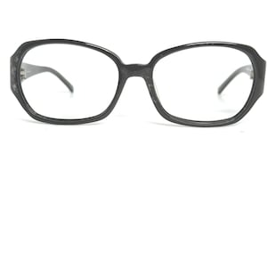 May include: Black, oversized eyeglasses with a rounded rectangular frame. The glasses have a dark, matte finish and feature a classic design. The lenses are clear, and the temples are thin and dark.