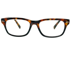 May include: Tortoiseshell pattern eyeglasses. The frames are rectangular with rounded edges and black rims. Small white dots are on the outer corners. The lenses are clear.