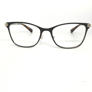 May include: Black eyeglasses with a cat-eye frame. The glasses have a thin, dark frame with a gold accent on the temples and brown tortoise shell arms. The lenses are clear.