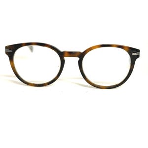 May include: Round eyeglasses with a tortoiseshell pattern. The frames are brown and black with clear lenses. The glasses have a keyhole bridge and a modern design.