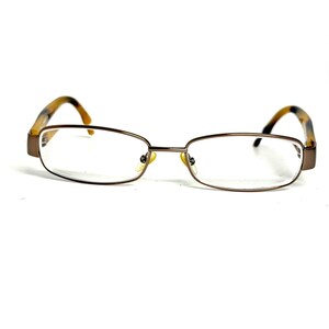 May include: Rectangular eyeglasses featuring a thin, metallic bronze-toned frame. The temples are crafted with a mottled brown and black tortoiseshell pattern. The bridge connects two clear lenses, and the nose pads are visible in a light gold tone.