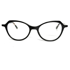 May include: Black oval-shaped eyeglasses with a unique frame design. The glasses have a glossy finish and clear lenses. The temples feature a subtle patterned detail. The overall style is modern and sophisticated, suitable for everyday wear.