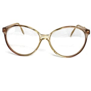 May include: A pair of round, clear, plastic spectacles with a gold-toned frame.