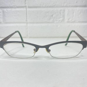May include: A pair of brown metal eyeglasses with green accents on the arms. The glasses have a cat-eye shape and clear lenses.