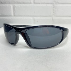 Pode incluir: Óculos de sol pretos com armação elegante e curva e lentes cinza escuras.