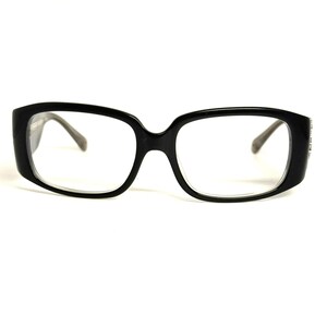 May include: Black rectangular eyeglasses with clear lenses and a thick, solid frame. The glasses feature a smooth, glossy finish on the front and sides, with a bridge connecting the two lenses. The temples extend outward from the frame corners.