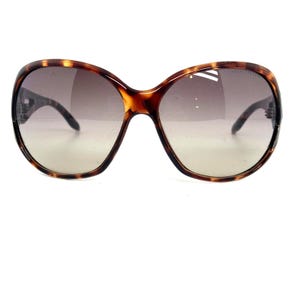 Può includere: Occhiali da sole tartaruga con lenti marroni sfumate. Gli occhiali hanno una montatura rotonda e oversize.