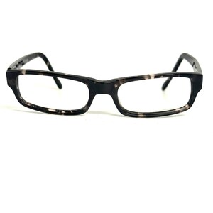Pode incluir: Óculos retangulares com uma armação de padrão tartaruga em cinzento escuro e branco. Os óculos possuem hastes finas e retas e uma ponte que liga as duas lentes, proporcionando uma visão clara da estrutura e do design da armação.