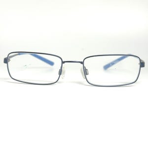 May include: Rectangular eyeglasses featuring a thin dark navy blue metal frame. The temples are accented with bright blue interior detailing. The clear lenses are held in place by a slim bridge and adjustable transparent nose pads for support.