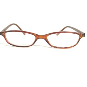 May include: A pair of eyeglasses with a brown frame and clear lenses. The glasses have a rectangular shape with rounded edges. The temples are a darker brown color.