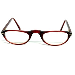 Può includere: Un paio di occhiali vintage con montatura rosso scuro e lenti trasparenti. Le lenti ovali sono inserite in un design elegante e minimalista. Le aste sono di colore rosso scuro abbinato.
