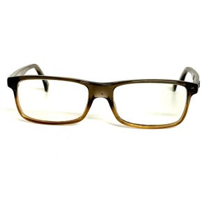 May include: Rectangular eyeglasses featuring a gradient frame that transitions from a dark brown at the top to a lighter, translucent amber tone at the bottom. The glasses have thin, clear lenses and integrated nose pads, with dark brown temples extending outward.