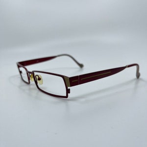 May include: Burgundy-colored metal eyeglasses with gold accents. The glasses have a rectangular frame and thin arms.