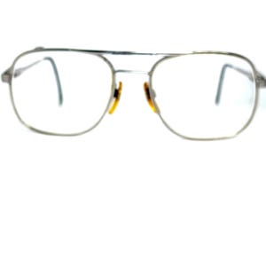 May include: Silver-framed aviator eyeglasses with clear lenses. The glasses have a double bridge and a classic design. The nose pads are a light brown color. The overall style is vintage and timeless.