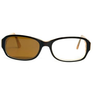 May include: Eyeglasses featuring a black frame with a light tan inner rim. The left lens is tinted a solid brown color, while the right lens is clear. The temples are a light tan color, and the overall design is a classic oval shape.
