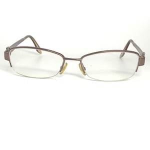 May include: A pair of eyeglasses with a brown metal frame and clear lenses. The glasses have a half-rim design, with the frame extending along the top and sides of the lenses. The earpieces are also brown.
