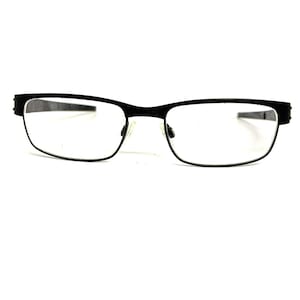May include: A pair of black rectangular eyeglasses featuring a thin frame design. The glasses have clear lenses and a bridge connecting the two rims. The temples extend outward from the sides of the frame, showcasing a simple and functional construction.