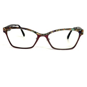 May include: Eyeglasses featuring a deep maroon frame with a distinct cat-eye shape. The upper rim is decorated with a multicolored, iridescent mosaic pattern in shades of teal, purple, and tan. The temples are thin and black, providing a contrast.