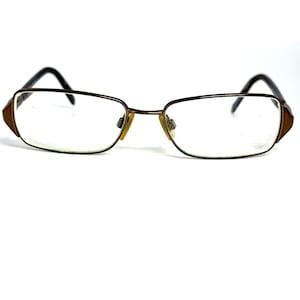 May include: Rectangular eyeglasses featuring a thin, metallic brown frame with clear lenses. The design includes dark brown temple arms and small, yellowish-toned nose pads, providing a structured look for these functional optical frames.