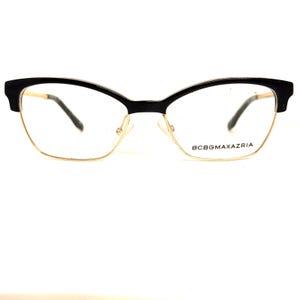 May include: Black cat-eye eyeglasses with gold metal frames and clear lenses. The brand name "BCBGMAXAZRIA" is printed on the right lens.