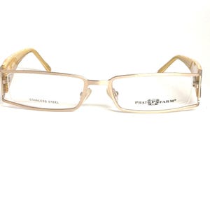 May include: Rectangular eyeglasses with a gold-colored metal frame. The temples have a striped pattern in shades of beige and gold. The text "STAINLESS STEEL" is visible on the left lens frame, and the "PHAT FARM" logo is on the right lens frame.