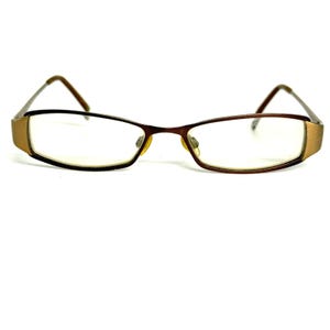 May include: Rectangular eyeglasses featuring a dark brown frame with metallic gold-toned accents on the outer edges. The glasses have clear lenses, a thin bridge, and adjustable nose pads, with slender brown arms extending from the sides.