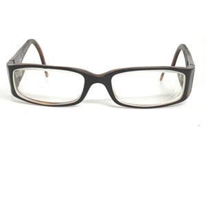 Peut inclure: Lunettes rectangulaires avec une monture noire et des branches marron. Les verres sont clairs et la monture présente un subtil accent marron autour des verres. Ces lunettes sont conçues pour la correction de la vue.