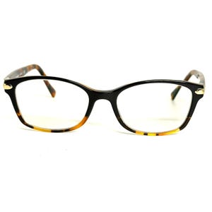 May include: Eyeglasses featuring a glossy black frame front that transitions into a brown and black tortoiseshell pattern on the lower rims and temples. The design includes small gold-toned metal accents at the hinges of the frame.