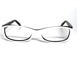 May include: A pair of eyeglasses featuring a thick white frame with a contrasting black inner rim. The glasses have a rectangular shape with slightly rounded edges and dark, thin temples extending from the sides of the front frame.