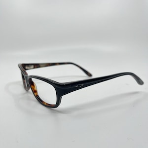 May include: Black and tortoise shell eyeglasses with a rectangular frame. The glasses have a sleek design with a small logo on the temples. The lenses are clear, and the arms curve gently for a comfortable fit. The glasses are set against a white background.