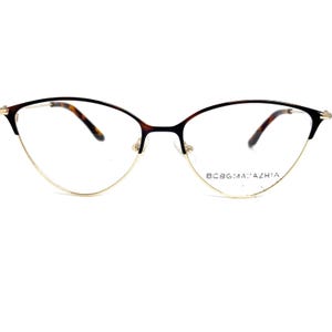 May include: A pair of tortoiseshell cat-eye eyeglasses with gold metal frames and clear lenses. The brand name "BCBGMAXAZRIA" is printed on the right lens.