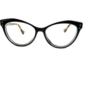 May include: Black cat-eye eyeglasses with clear lenses. The frames have a thick, glossy finish and feature small, decorative rivets on the outer corners. The inner arms have a tortoiseshell pattern.
