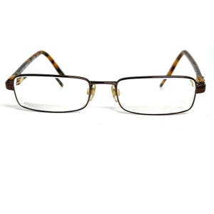 May include: Rectangular eyeglasses featuring a thin dark brown metal frame and clear lenses. The temples are accented with a mottled brown and black tortoiseshell pattern, and the nose pads are visible behind the bridge of the frame.
