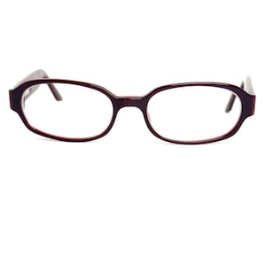 May include: Oval-framed spectacles in a deep burgundy hue. The lenses are clear, and the frame features a gentle, rounded design. The glasses are presented against a white backdrop, accentuating their colour and form.