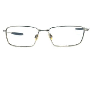 May include: Silver-coloured rectangular eyeglasses. The glasses feature a thin, wire frame and small nose pads. The lenses are clear, and the design is minimalist and modern. The frame is made of a metal.