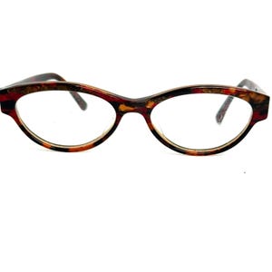 May include: A pair of eyeglasses with a tortoiseshell pattern. The frames are a mix of brown, red, and yellow, with a cat-eye shape. The lenses are clear, and the glasses are set against a white background.