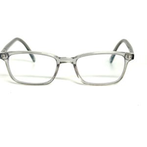 Może przedstawiać: Okulary z półprzezroczystą, jasnoszarą oprawką o prostokątnym kształcie. Okulary posiadają przezroczyste szkła oraz zakrzywione zauszniki, które wychodzą z zewnętrznych krawędzi oprawki, zapewniając prosty i funkcjonalny wygląd.