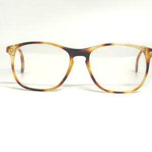 May include: A pair of eyeglasses with a tortoiseshell pattern on the frames. The frames are a mix of brown and tan colors. The lenses are clear and round. The glasses are set against a white background.