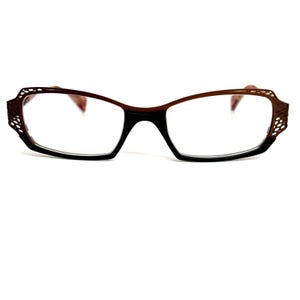 May include: Brown and black eyeglasses with a decorative frame. The frame has a geometric pattern.