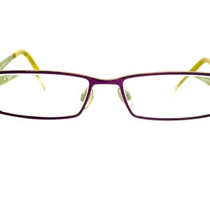 May include: Rectangular eyeglasses with a purple frame and gold accents. The lenses are clear, and the temples are a combination of green and yellow. The glasses have a modern, minimalist design.