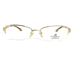 May include: Gold-tone metal eyeglasses with a semi-rimless frame design. The right lens features the text Catherine Deneuve LUNETTES DEMO LENS ONLY printed in black. The temples have a decorative textured pattern near the hinges.