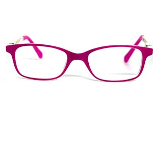 May include: A pair of magenta-colored eyeglasses with a rectangular frame. The temples are a lighter pink and connect to the frame with silver-colored accents. The lenses are clear, and the glasses are set against a white background.