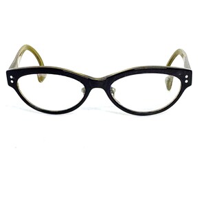 May include: Black cat-eye glasses with a green frame. The glasses have a clear lens.